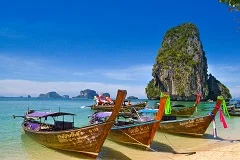 Krabi dramatic limestone karst cliffs rising from turquoise waters, Railay Beach with rock climbers on cliff face, longtail boats with colorful ribbons, pristine white sand beaches, tropical jungle, kayakers exploring caves and lagoons, Phi Phi Islands in distance, mangrove forests, sunset over Andaman Sea