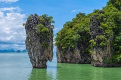 Phuket tropical beaches with turquoise waters and white sand, dramatic limestone karst islands in Phang Nga Bay, longtail boats on crystal clear water, Buddhist temples with golden spires, street food vendors, snorkeling with colorful fish, beachfront bars and restaurants, sunset over Andaman Sea, tropical jungle hills